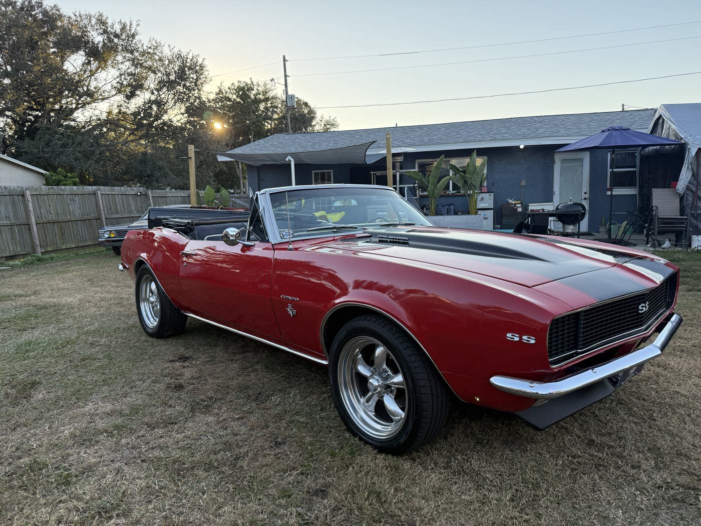 Red 1967 Camaro SS convertible with black stripes, parked on the grass at sunset